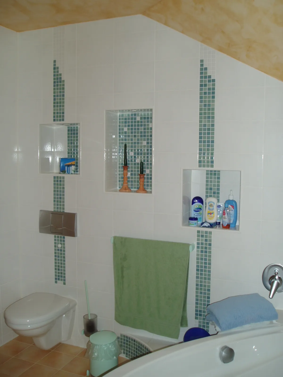 Badezimmer mit weißen Wandfliesen und türkisfarbenen Mosaikstreifen als Akzente